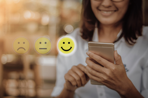 Imagen de una mujer dándole una carita feliz a una compra mediante su celular haciendo referencia a la satisfacción del cliente.